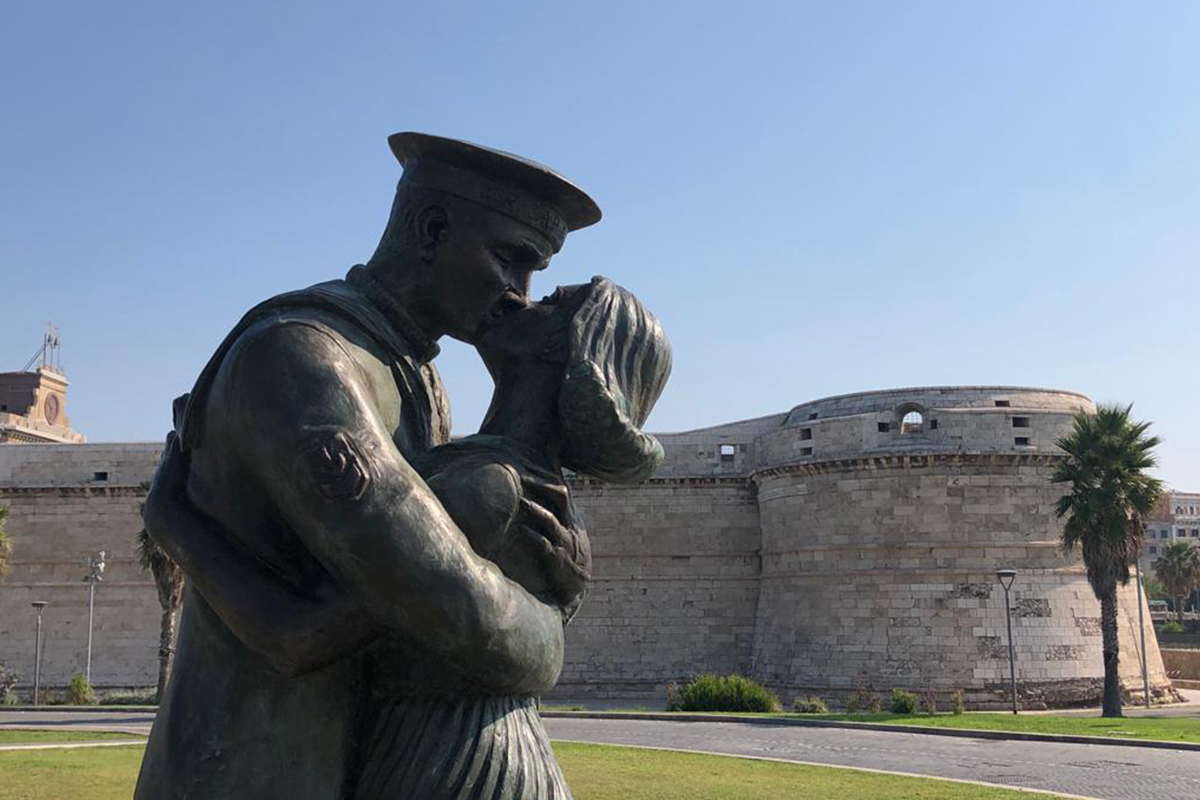 La estatua “El beso en la memoria de un puerto”. En el fondo, el Fuerte Michelangelo.